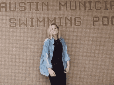 a woman in a denim jacket is standing in front of a sign for the austin municipal swimming pool