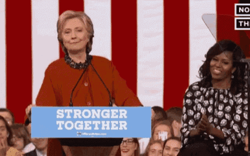 hillary clinton stands behind a podium with a sign that says stronger together
