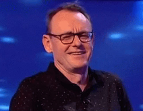 a man wearing glasses and a black shirt is smiling and looking at the camera .