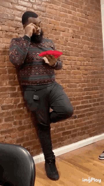 a man leans against a brick wall while holding a red object