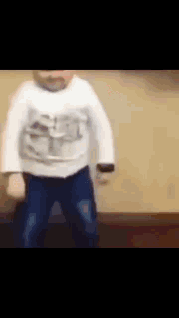 a baby in a white shirt and blue jeans is standing on a wooden floor .