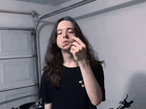 a young man with long hair is smoking a cigarette in a garage