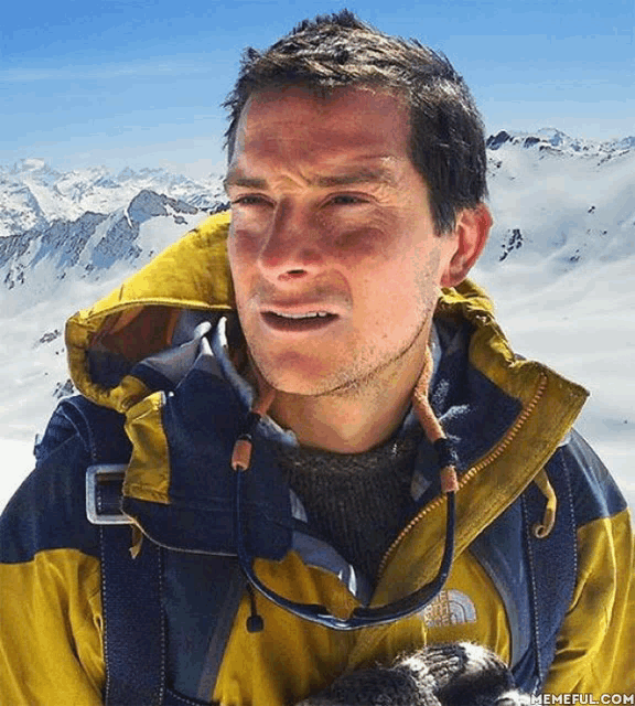a man wearing a yellow and blue north face jacket stands in front of a snowy mountain