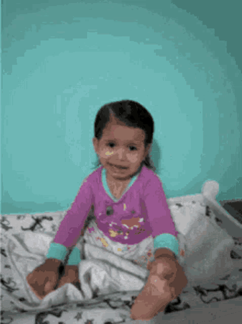 a little girl in a purple shirt is sitting on a bed with her eyes closed