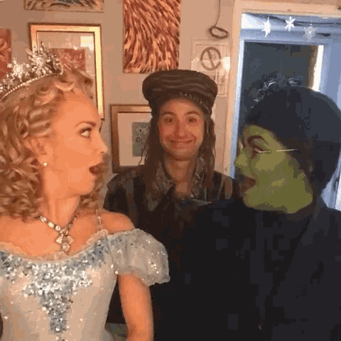 a woman in a blue dress is standing next to a man in a hat and a woman in a green mask