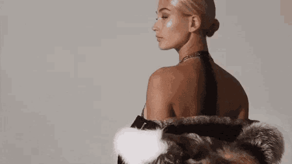 a woman wearing a fur coat and a necklace is standing in front of a white wall .
