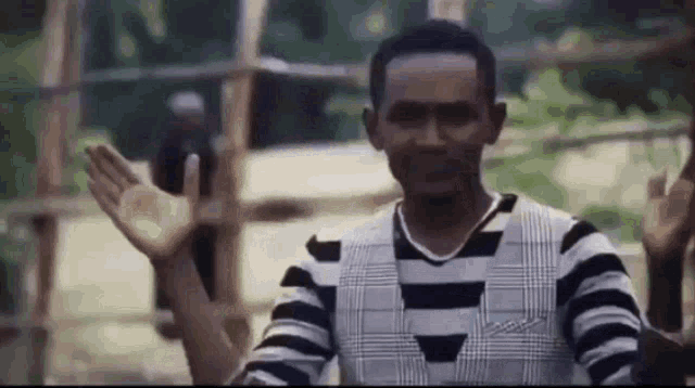 a man in a striped shirt is waving his hand in front of a group of people .