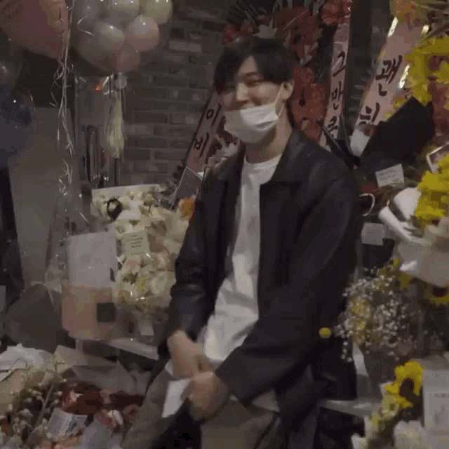 a man wearing a face mask is sitting in front of a table full of flowers and balloons