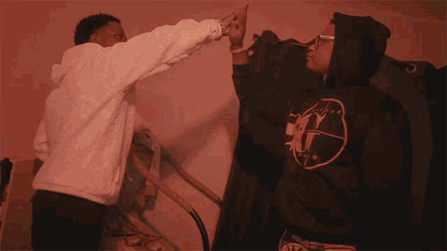 a man in a white hoodie is reaching out towards a black hoodie with the letter g on the back