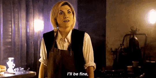 a woman in an apron is standing in a dark room and talking to someone .