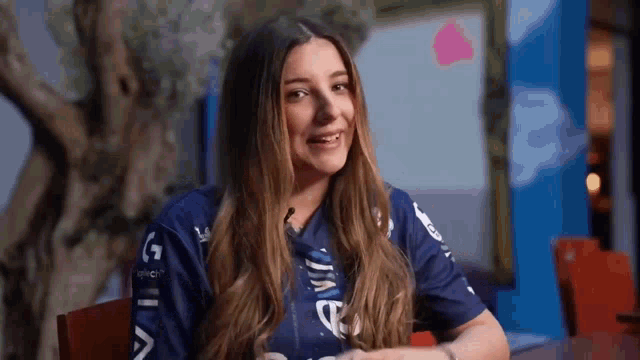 a woman in a blue shirt is sitting at a table with a microphone in her mouth .