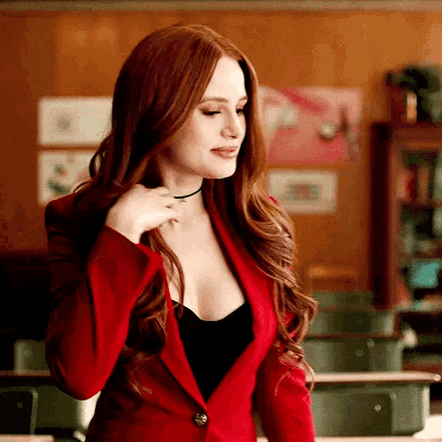 a woman with long red hair is wearing a red jacket and a black top .