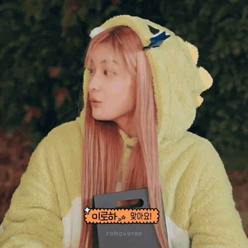 a woman with pink hair is wearing a green hoodie with a sticker that says rohaverse
