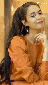 a woman in an orange dress is sitting down with her hand on her chin and looking at the camera .