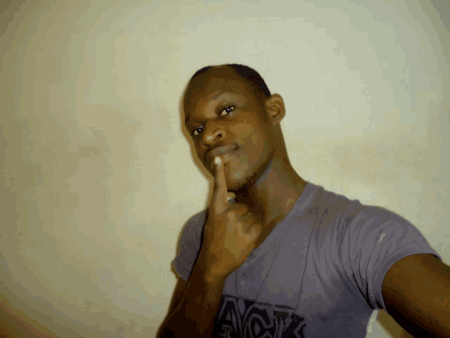 a man wearing a grey shirt that says avok holds his finger to his chin