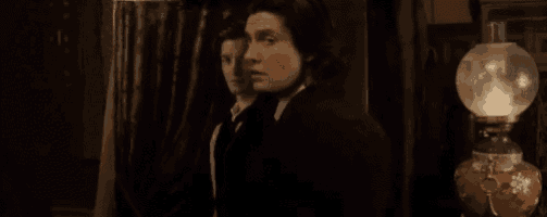 two men are standing next to each other in a dark room with a lamp in the background .