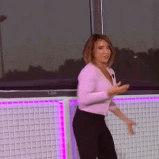 a woman in a pink sweater and black pants is dancing in front of a window