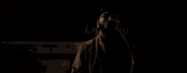 a man in a hat is standing in the dark in front of a sign that says lighting and car .
