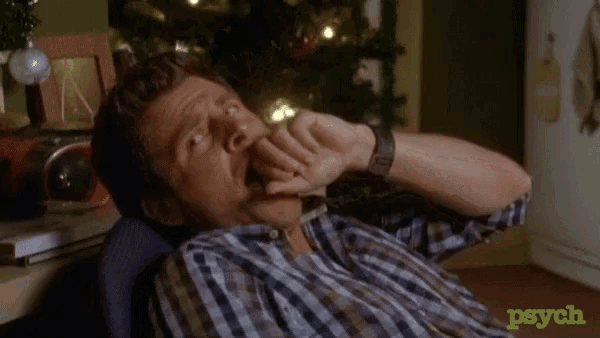 a man in a plaid shirt is sitting in front of a christmas tree and yawning .