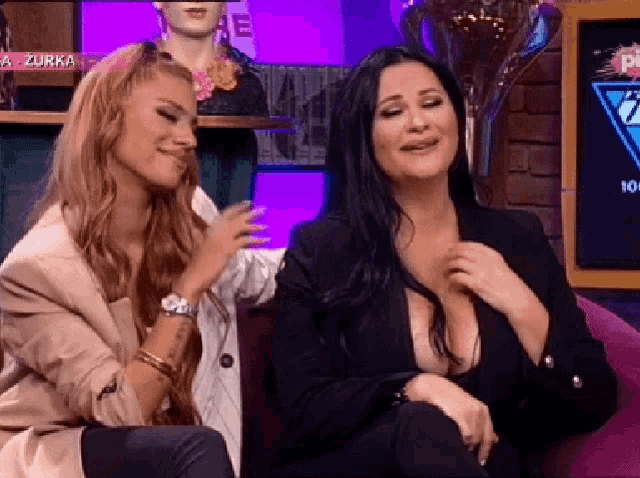 two women are sitting next to each other on a couch and one of them has a very large cleavage .
