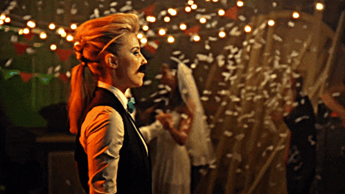 a woman in a tuxedo with a mustache is standing in front of confetti