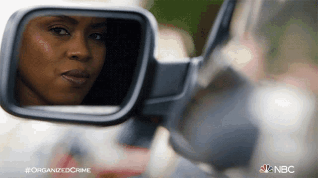 a woman is reflected in the rear view mirror of a car with the hashtag organized crime