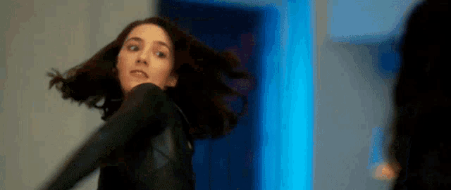 a woman in a black jacket is standing in front of a blue light .