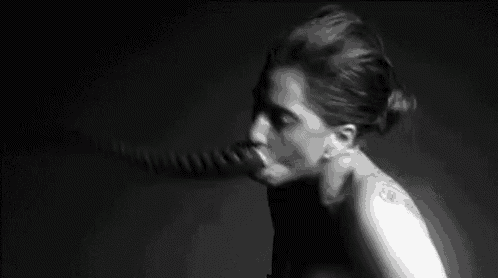 a black and white photo of a woman sucking a large carrot .
