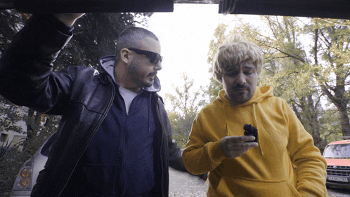 a man in a yellow hoodie is holding a cell phone