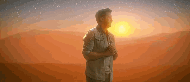 a man standing in front of a sunset with his hands folded in prayer .