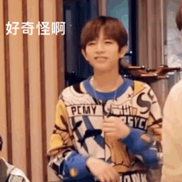 a young man wearing a sweater that says pcmy is standing in front of a group of people .