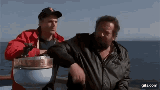a man in a red jacket is standing next to a man in a black jacket on a boat .