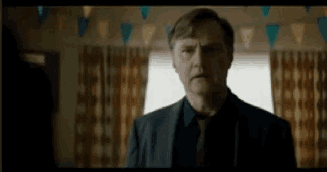 a man in a suit and tie is standing in a room with curtains and flags .