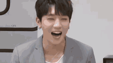 a young man in a suit is laughing with his eyes closed and his mouth open .