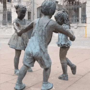a statue of a boy and two girls playing with each other on a sidewalk