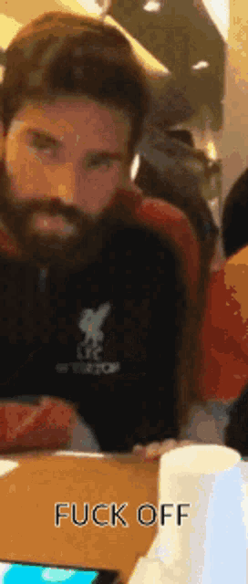 a man with a beard is sitting at a table with the words " fuck off " on the bottom