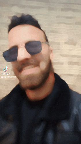 a man with a beard wearing sunglasses and a black jacket has a tiktok sticker on his face
