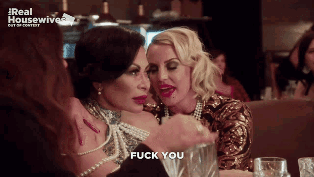 two women are sitting at a table and one says fuck you