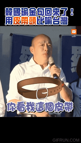 a man holding a microphone with a belt in front of him with chinese writing behind him