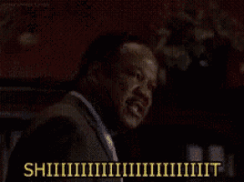 a man in a suit is screaming in a dark room with the words shhhh written in yellow