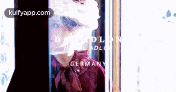 a woman in a red shirt is standing in front of a bottle of perfume made in germany .