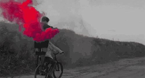 a man is riding a bike on a dirt road with red smoke coming out of his hand .