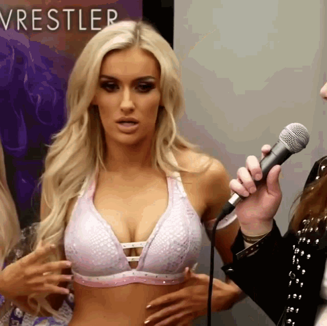 a woman in a bra is being interviewed by a man holding a microphone in front of a poster that says wrestler