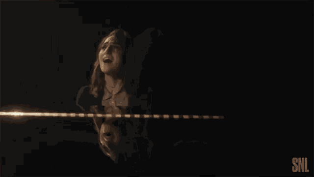 a woman is singing into a microphone in a dark room with a snl logo in the corner