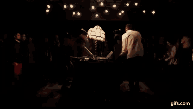 a group of people are dancing in a dark room with a lamp in the middle .