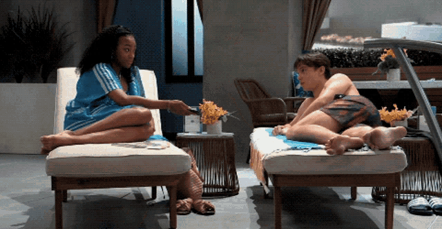 a woman sits on a lounge chair while a man lays on a lounge chair