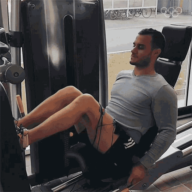 a man in a gray shirt is using a leg press machine in a gym