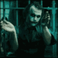 the joker from the movie the dark knight is holding his hands together in a dark room .