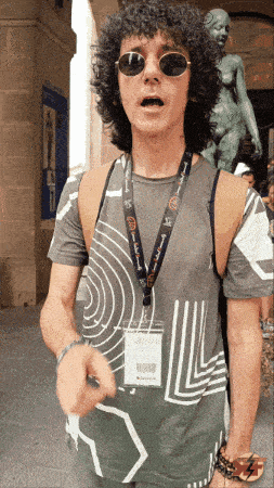 a man with curly hair wearing sunglasses and a lanyard that says ' a few words ' on it