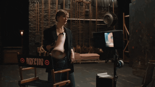 a woman stands in front of a director 's chair in a dark room